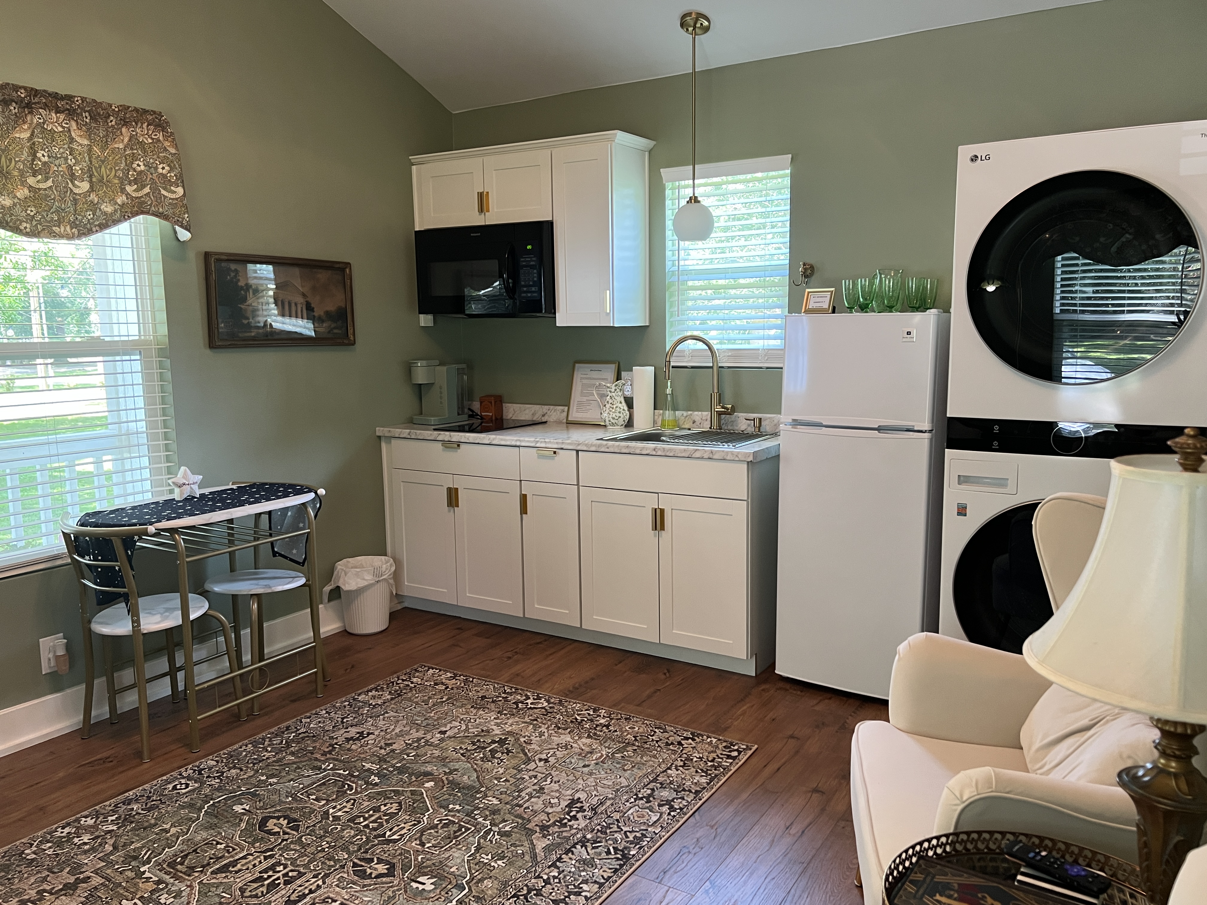 A modern kitchenette with sage green walls, white cabinets, a speckled counter, a black microwave, and gold hardware and fixtures.
