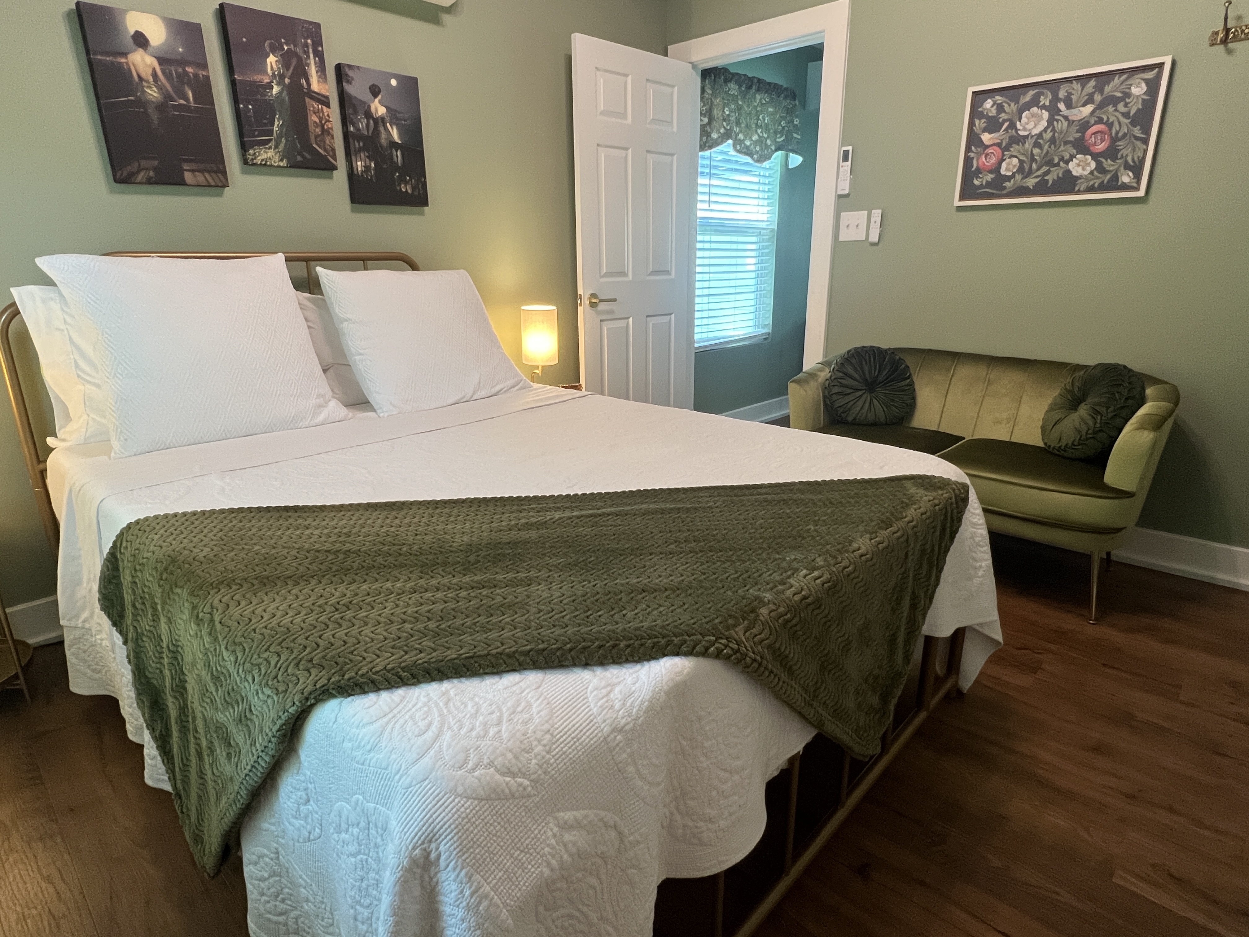 A cozy bedroom with sage green walls, queen size bed with white linens..