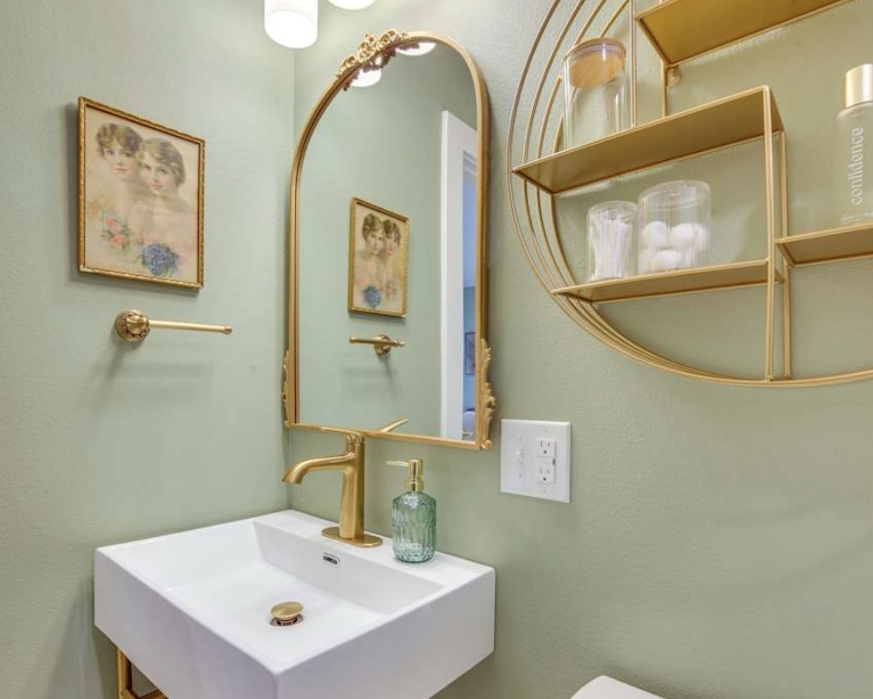 A chic bathroom with sage green walls, a white floating sink, an arched gold mirror, a matching gold faucet and towel ring, and circular shelving.