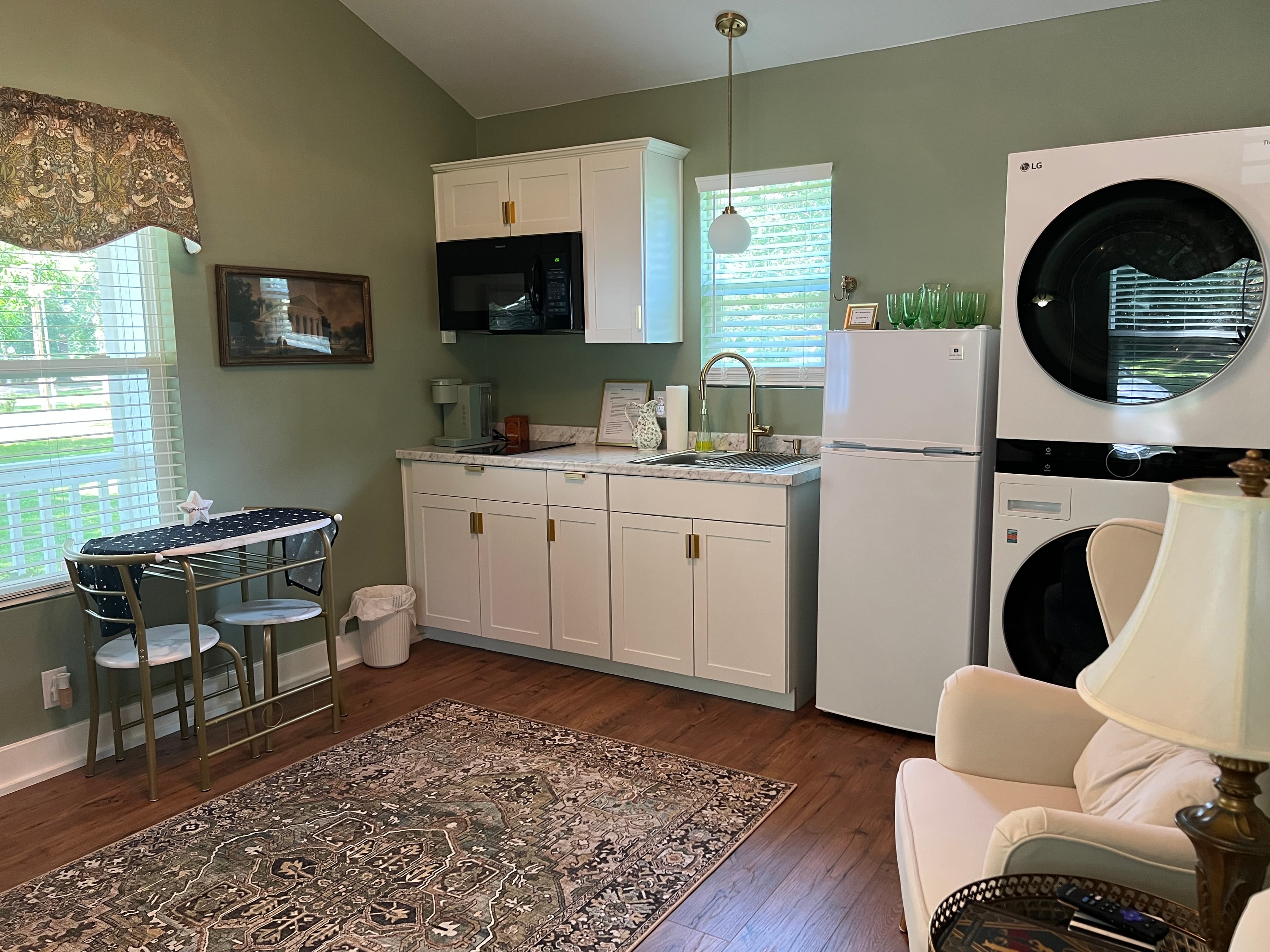 A modern kitchenette with sage green walls, white cabinets, a speckled counter, a black microwave, and gold hardware and fixtures.
