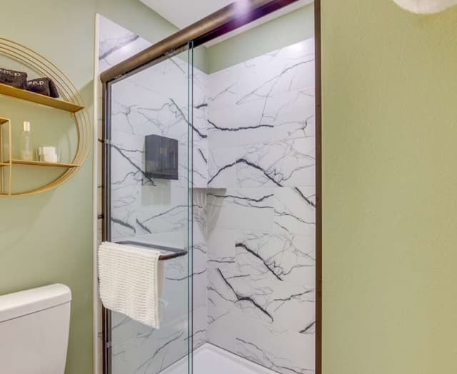 A modern walk-in shower with glass sliding doors, white and black marble-look tile on the walls, and sage green paint.