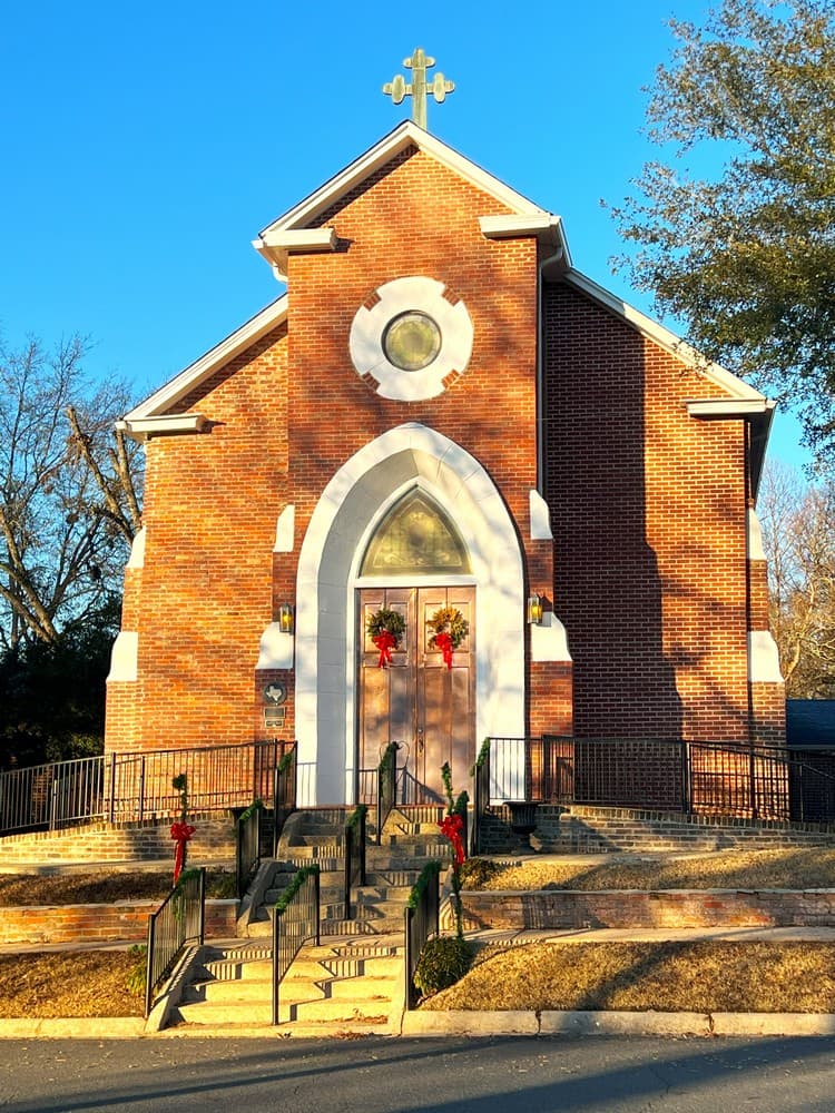 A brick church adorned with holiday wreaths and a cross, set against a clear blue sky.