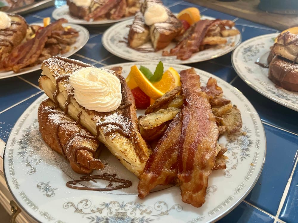 A plate of French toast topped with whipped cream, bacon, and fresh fruit.