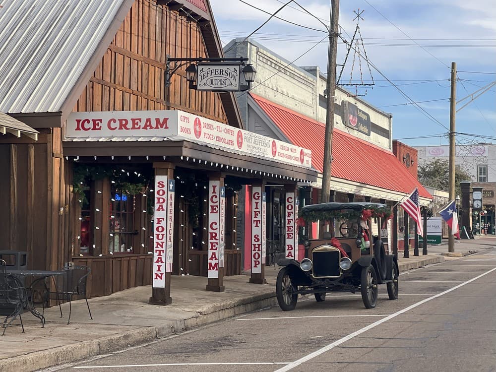 A vintage car is parked outside a charming ice cream shop with festive signage in a small town street. A vintage car is parked outside a charming ice cream shop with festive signage in a small town street.